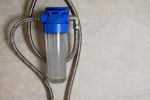 This image shows a water softener system with metal piping and a blue plastic top attached to a tiled internal wall.