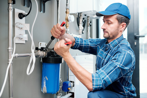 This image shows a plumber using a tool to install a water filter in a home's plumbing system.