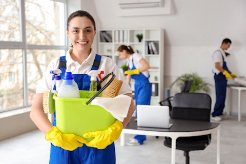 A cleaning lady is holding her supplies with cleaning team in the background