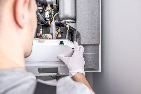 A worker opens a central heating furnace. Angle from behind.