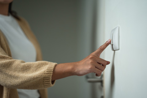 Closeup of a woman in a sweater’s hand on a light switch.
