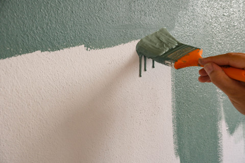 Closeup of a hand using a brush to paint a primed wall sage green.