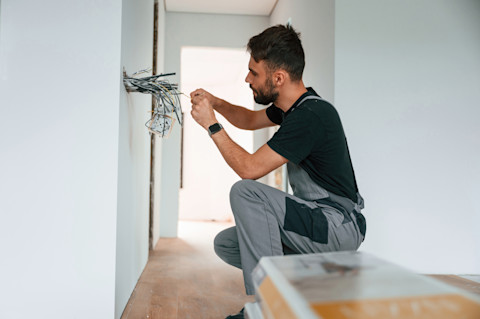 A man is installing electrical wiring in a new home.