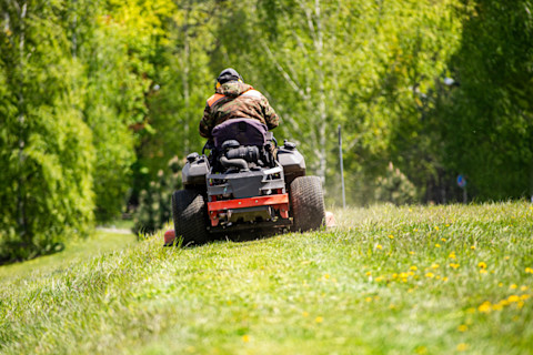 Lawn care specialist rides a tractor, leaving a trail of cut grass behind.