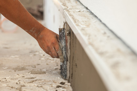 This image shows a close up of a hand using a tool to smooth a cement-type mixture over the crack in a building foundation.