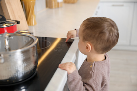 A toddler pushes a button on the control panel of a stovetop.