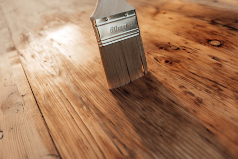 Close up of a brush passing over a shiny wooden surface while applying finish.