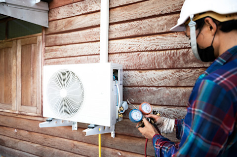 Outside a house, a workers installs and refills the exterior part of an air conditioning unit.