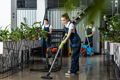 This image shows professional cleaners using a vacuum cleaner and mop to clean a modern office building.