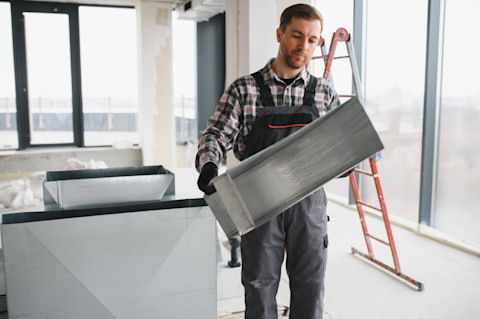 An HVAC technician assembles rectangular sheet metal ventilation ducts on-site during a home construction project.
