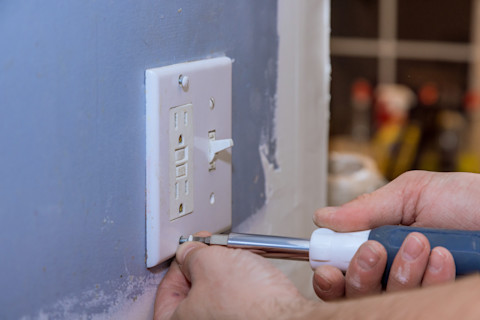 Closeup of a hand using a screwdriver on a light switch/electrical outlet.