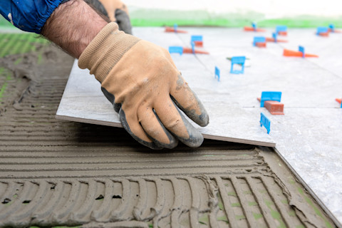 A bricklayer places tiles on a new floor surface. The tiles are aligned carefully with adhesive.