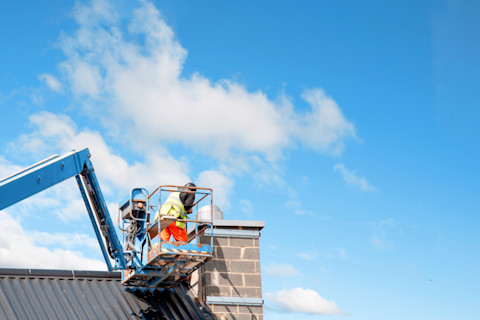 This image shows tradespeople in the basket of a crane fixing the chimney on a rooftop.