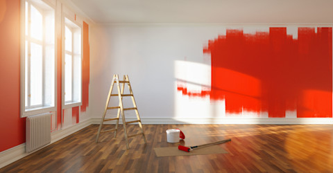 A man paints an interior wall red inside an apartment. The room appears freshly renovated with clean surfaces.