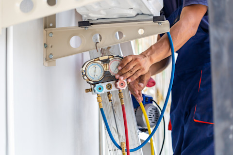 A technician fixes an air conditioning unit and checks the level of refrigerant.