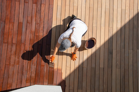 This image shows a tradesperson applying wood sealing protection to decking boards.