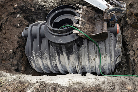 This image shows a black plastic in the ground with a green hose pipe leading into it.
