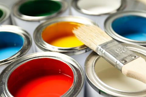 Closeup of several open cans of paint with a paintbrush lying on top.