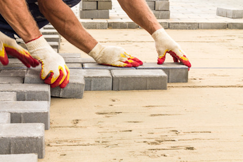 Workers lay paving tiles during outdoor construction. The area is partially completed.