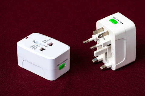 Closeup of two electrical converters for many different sockets on a dark red rug.