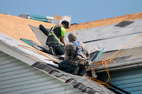This image shows two professional roofers installing roof tiles on the roof of a residential property.