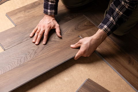 Closeup of a worker’s hands installing vinyl wood flooring over a smooth subfloor.