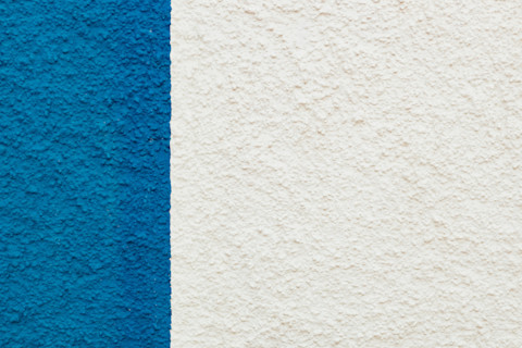 Full-frame shot of a stucco surface, mostly white with one bold blue rectangular section on the left.