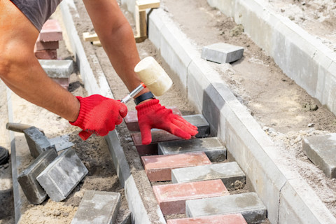 Paving contractor lays stones on a new pathway. The ground is prepared for even placement.