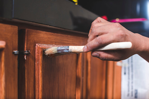 Closeup of a painter’s hand applying finish to wooden cabinets.