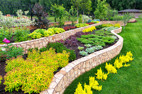 A beautiful border in a yard with flowers and plants in it on a grass field.